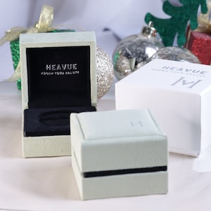 K&ouml;nnte beinhalten: Zwei gr&uuml;ne und wei&szlig;e Schmuckboxen mit dem Text "Heavue Adorn Your Beauty" auf der Oberseite. Die Boxen stehen auf einer wei&szlig;en Oberfl&auml;che.