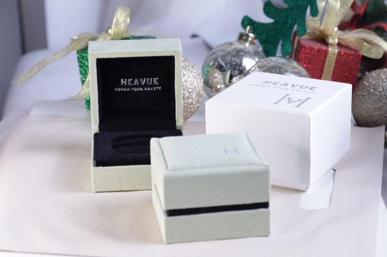K&ouml;nnte beinhalten: Zwei gr&uuml;ne und wei&szlig;e Schmuckboxen mit dem Text "Heavue Adorn Your Beauty" auf der Oberseite. Die Boxen stehen auf einer wei&szlig;en Oberfl&auml;che.