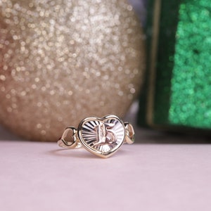 Puede incluir: Un anillo de oro en forma de coraz&oacute;n con el n&uacute;mero "15" grabado en el interior. El anillo est&aacute; rodeado por dos corazones m&aacute;s peque&ntilde;os a cada lado.