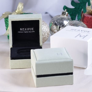 Puede incluir: Dos cajas de joyer&iacute;a verde y blanca con el texto "Heavue Adorn Your Beauty" en la parte superior. Las cajas est&aacute;n sobre una superficie blanca.