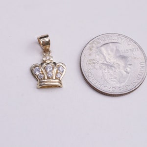 May include: A gold crown pendant with clear cubic zirconia stones. The pendant is about the size of a US quarter.