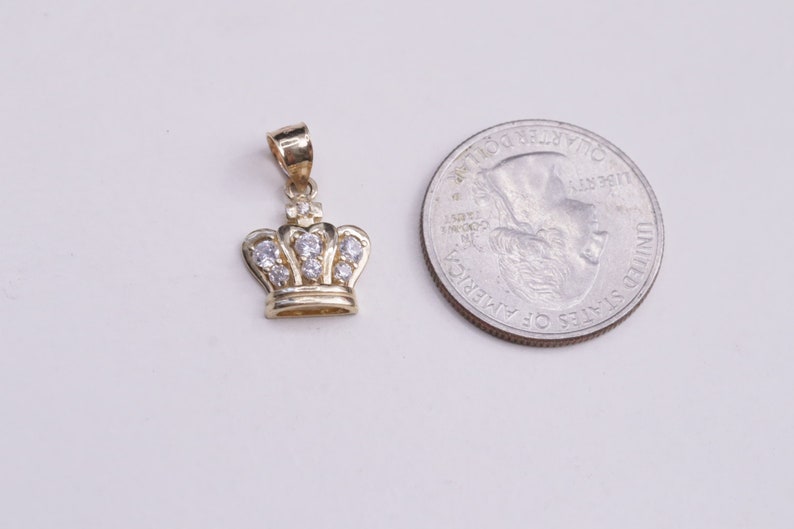 May include: A gold crown pendant with clear cubic zirconia stones. The pendant is about the size of a US quarter.
