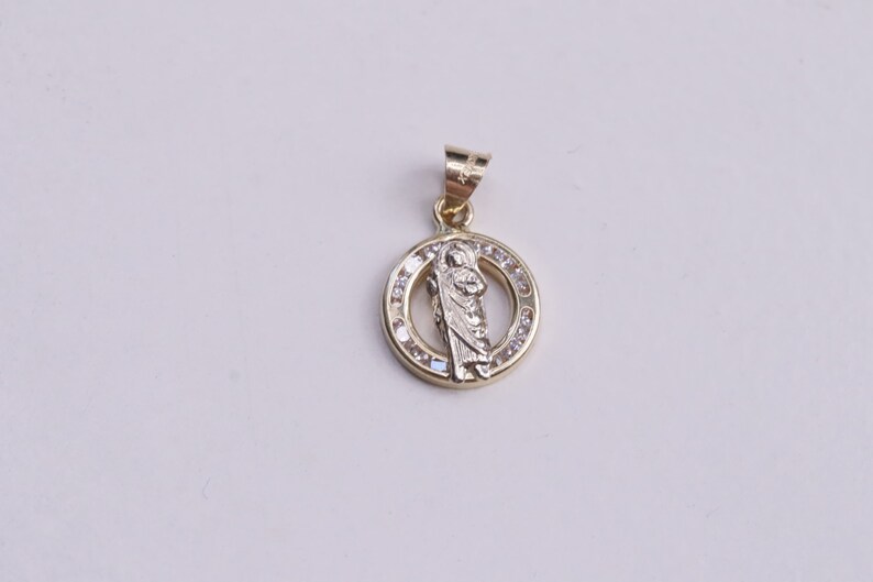 May include: A gold pendant with a religious figure in the center surrounded by clear stones.