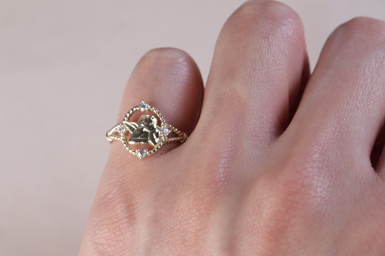 K&ouml;nnte beinhalten: Goldring mit einem kleinen Engelsmotiv und klaren Zirkonia-Steinen.