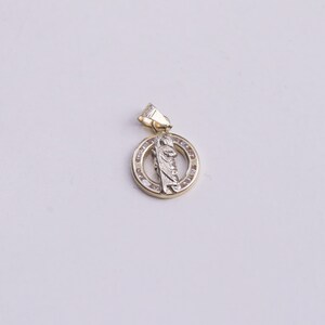May include: A gold pendant with a white figure in the center, surrounded by a circle of small clear stones.