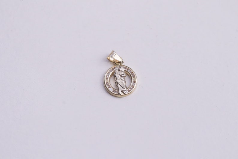 May include: A gold pendant with a white figure in the center, surrounded by a circle of small clear stones.