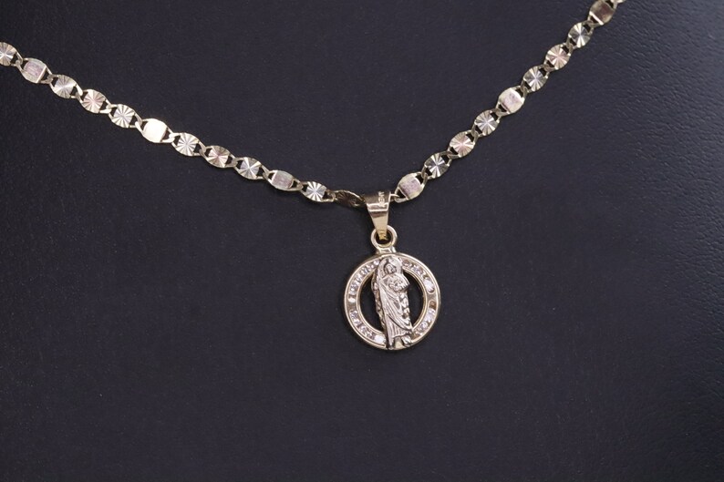 May include: A gold chain necklace with a pendant featuring a religious figure in a circle with small clear stones around the edge.