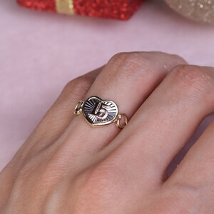 Puede incluir: Anillo de oro en forma de coraz&oacute;n con el n&uacute;mero "15" grabado en el interior. El anillo est&aacute; en un dedo.