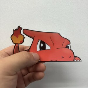 Puede incluir: Un personaje de dibujos animados rojo con una llama en la cola, asomándose desde detrás de una superficie blanca. El personaje tiene una expresión feroz y un solo ojo negro.