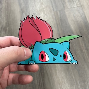 May include: A blue and green cartoon character with red eyes peeking out from behind a red flower. The character is a sticker.