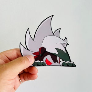 Op de afbeelding: Een wit en groen cartoonfiguur met rode ogen die vanuit een witte ondergrond kijkt. Het figuur heeft een zwart-rode sjaal om zijn nek.