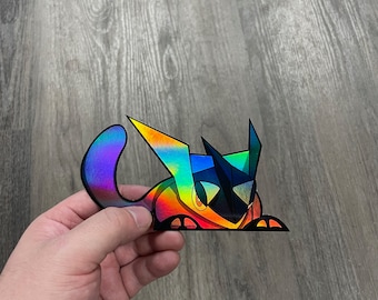 May include: A holographic sticker of a cartoon creature with a blue, black, and yellow color scheme. The creature has a pointed head and a long tail.