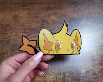 May include: A yellow sticker of a cartoon character with a star-shaped marking and a star-shaped accessory. The sticker has black outlines and is held against a wooden background.