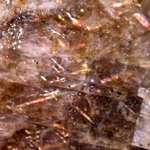 K&ouml;nnte beinhalten: Nahaufnahme eines Sunstone, einer Feldspatart, mit durchscheinender, hellbrauner Farbe und irisierenden Blitzen von Rot, Orange, Gelb und Gr&uuml;n.
