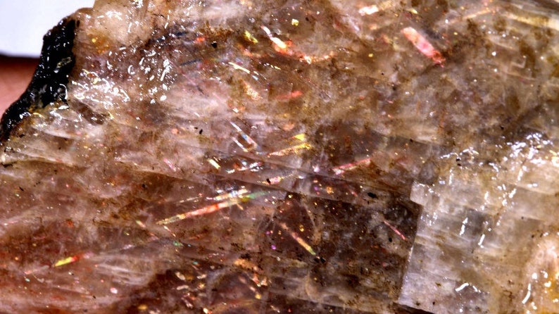 K&ouml;nnte beinhalten: Nahaufnahme eines Sunstone, einer Feldspatart, mit durchscheinender, hellbrauner Farbe und irisierenden Blitzen von Rot, Orange, Gelb und Gr&uuml;n.