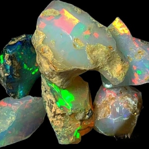 Könnte beinhalten: Eine Gruppe von rohen Opal-Steinen in verschiedenen Farben, darunter Grün, Blau und Rot. Die Steine haben verschiedene Formen und Größen.