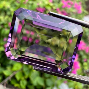 May include: A large, emerald-cut amethyst gemstone with a purple and green colour gradient. The gemstone is faceted and has a high degree of clarity.