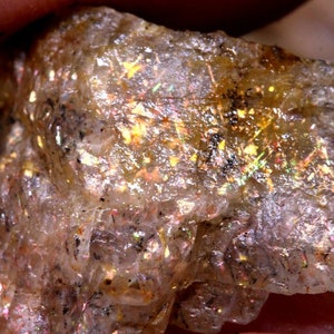 以下が含まれることがあります： 金色に輝く、ざらざらとした半透明の虹色のサンストーン。石は自然で、生々しい外観で、目に見える内包物を含んでいます。