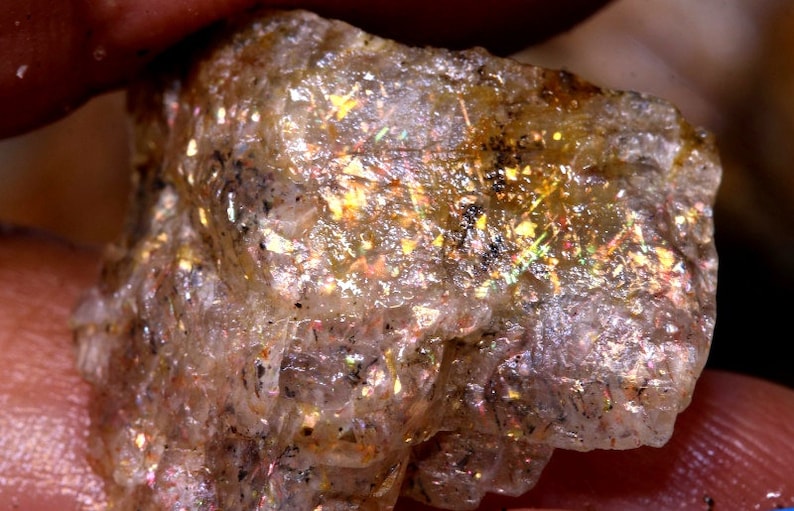K&ouml;nnte beinhalten: Ein rauer, durchscheinender, irisierender Sunstone mit goldenem Schimmer. Der Stein hat ein nat&uuml;rliches, rohes Aussehen mit sichtbaren Einschl&uuml;ssen.