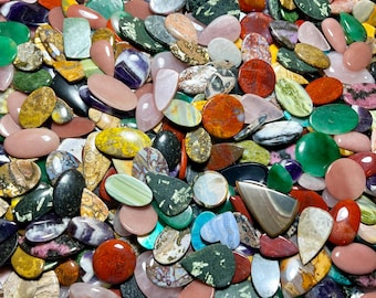 Peut inclure: Un assortiment de pierres précieuses polies de différentes formes et couleurs, dont ovales, en forme de goutte et rondes. Les pierres précieuses sont un mélange de rouge, vert, violet, jaune et noir, avec des motifs et des textures uniques. L'image présente une variété de pierres naturelles.