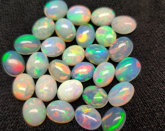 Puede incluir: Una colección de piedras preciosas de ópalo de forma ovalada en varios tonos de blanco, con destellos iridiscentes de color, incluyendo verde, azul, rosa y naranja.
