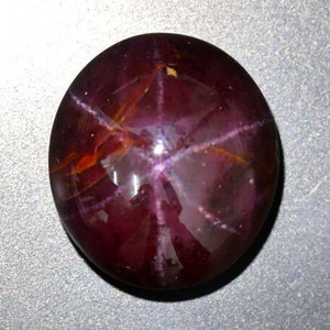 May include: A deep red star ruby cabochon gemstone with a six-pointed star in the center.