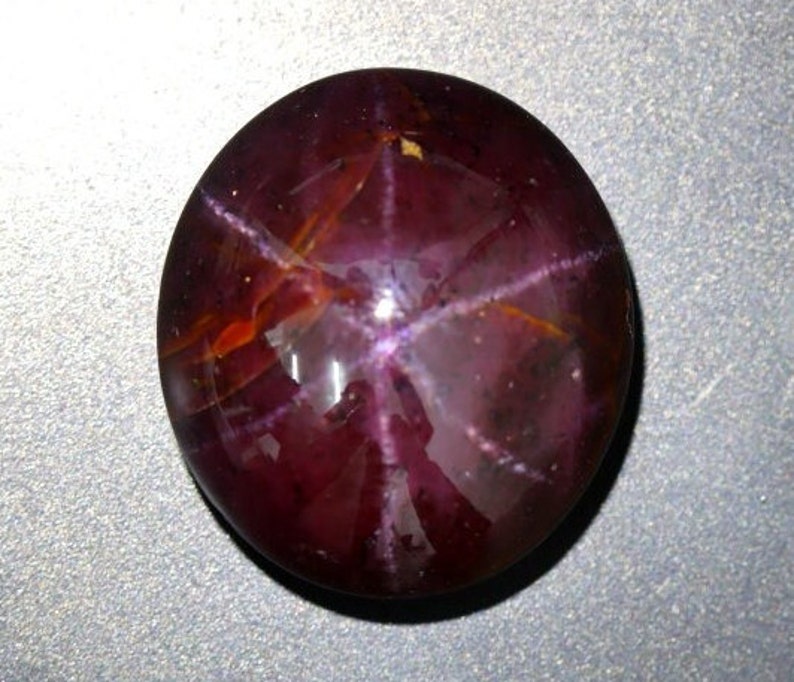 May include: A deep red star ruby cabochon gemstone with a six-pointed star in the center.
