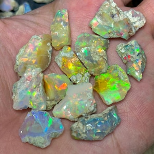 Peut inclure: Plusieurs opales brutes, présentant un éventail de couleurs, dont le vert, le jaune et le bleu. Les opales ont un aspect brut et naturel, avec une matrice visible. Les pierres précieuses sont tenues dans une main, soulignant leur taille et leur texture.