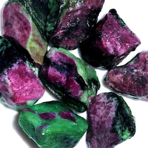 May include: A collection of seven rough, natural, green, pink, and black gemstones. The stones are tumbled and have a smooth, polished surface.