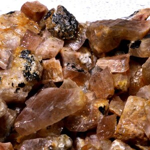 K&ouml;nnte beinhalten: Nahaufnahme eines Haufens rohen Sunstone, der die nat&uuml;rliche, rohe Sch&ouml;nheit des Edelsteins zeigt. Der Sunstone ist eine Mischung aus orange, rosa und braunen Farbt&ouml;nen, wobei einige St&uuml;cke einen leichten Schimmer haben.