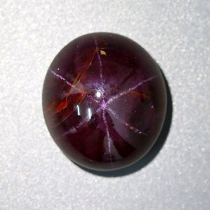 May include: A deep red star ruby cabochon gemstone with a six-pointed star pattern.