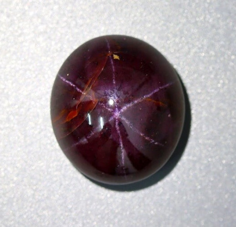 May include: A deep red star ruby cabochon gemstone with a six-pointed star pattern.