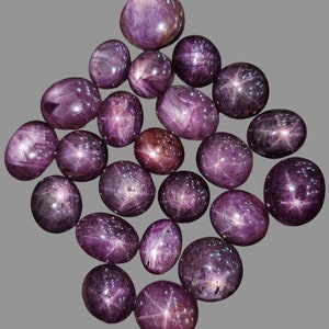 Può includere: Una collezione di 20 zaffiri stellati viola, ognuno con una stella a sei punte al centro. Le pietre sono di forma ovale e hanno una finitura liscia e lucida.