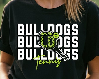 May include: Black t-shirt with the text "BULLDOGS TENNIS" in white and neon green. The design includes a tennis racket and ball. The shirt is worn by a person in a stadium setting.