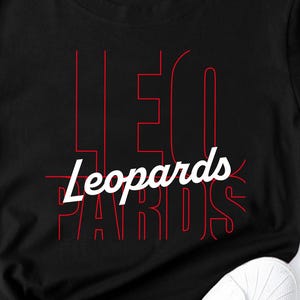 May include: Black t-shirt with the word "Leopards" in white script and red outlined text. The shirt is styled with a knot at the waist and paired with white sneakers. The overall aesthetic is casual and modern.