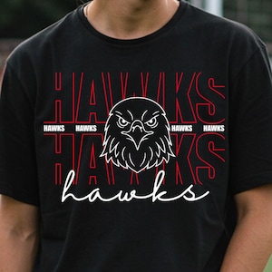 May include: Black t-shirt with a white hawk head graphic and the word "hawks" in a script font. The word "hawks" is also printed in red block letters above the hawk graphic.