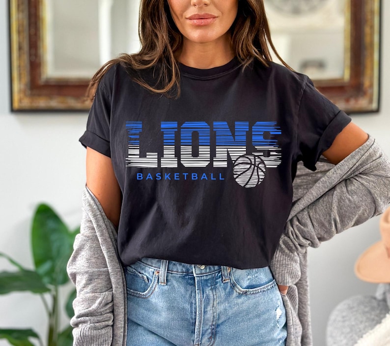 May include: Black t-shirt with a graphic of the word "LIONS" in white with blue stripes and a basketball graphic. The text "BASKETBALL" is below the graphic.