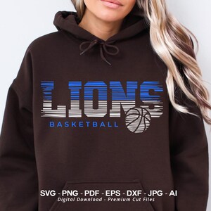 May include: A brown hoodie with a graphic design of the word "LIONS" in blue and white stripes with a basketball underneath. The text "BASKETBALL" is below the graphic.