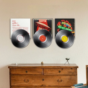 Puede incluir: Tres discos de vinilo exhibidos en una pared, cada uno con una portada de álbum diferente. El primero presenta texto de Mac Miller, el segundo tiene un diseño "Mothership" de Led Zeppelin y el tercero muestra un letrero de neón para Red Hot Chili Peppers.