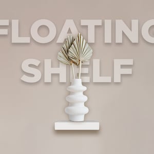 May include: A white floating shelf with a white, decorative vase holding dried palm leaves. The vase has a unique, layered design. The words "FLOATING SHELF" are displayed above the shelf in large, block letters.