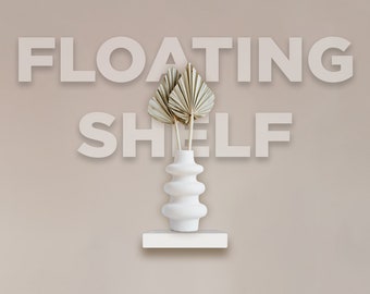 May include: A white floating shelf with a white, decorative vase holding dried palm leaves. The vase has a unique, layered design. The words "FLOATING SHELF" are displayed above the shelf in large, block letters.