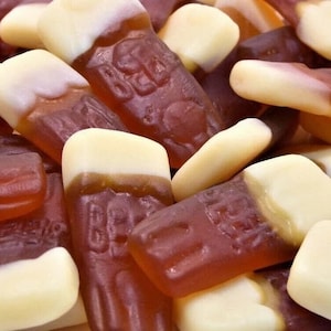 May include: A close-up of a pile of brown and white gummy sweets shaped like bottles of fizzy pop. The sweets have a realistic texture and are perfect for a sweet treat.