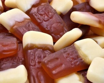 Puede incluir: Primer plano de un montón de caramelos gomosos marrones y blancos con forma de botellas de refresco. Los caramelos tienen una textura realista y son perfectos para un dulce capricho.