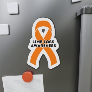 Puede incluir: Cinta naranja con el texto "LIMB LOSS AWARENESS" sobre un fondo blanco. La cinta está en un refrigerador plateado.