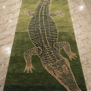 Puede incluir: Una alfombra rectangular verde con un diseño detallado de un caimán. El caimán está representado en un tono más claro, con patrones intrincados y una apariencia texturizada. Adecuado para una sala de estar o entrada.