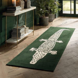 Puede incluir: Una alfombra rectangular verde con un gran diseño de cocodrilo blanco. La alfombra está colocada sobre un suelo de madera. Un elemento decorativo para salón o dormitorio.