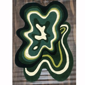 May include: Abstract green and cream rug with a layered, organic shape. The rug has a unique, modern design.