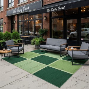 Può includere: Set da patio all'aperto con un tappeto a scacchi verde e verde chiaro. Il set comprende un divano, due poltrone e due piccoli tavolini in legno. Le sedie e il divano hanno cuscini grigi e telai in metallo nero. Il tappeto è etichettato "Woven Craft".