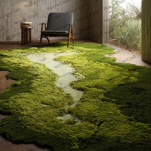 May include: A large, green moss rug with a lighter, river-like design running through the center. The rug is placed on a wooden floor, with a modern chair and side table in the background. The room has a natural, earthy aesthetic.