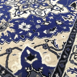 May include: Close-up of a blue and beige patterned rug. The rug features a central design with floral and geometric motifs in shades of blue, beige, and white. The border has a repeating floral pattern. The rug is made of a soft, woven material.